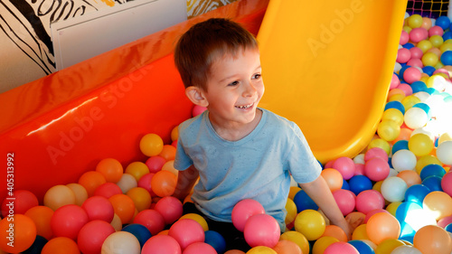 Happy laughing little boy riding down the slide on children palyground and diving in pool with colorful plastic balls. photo