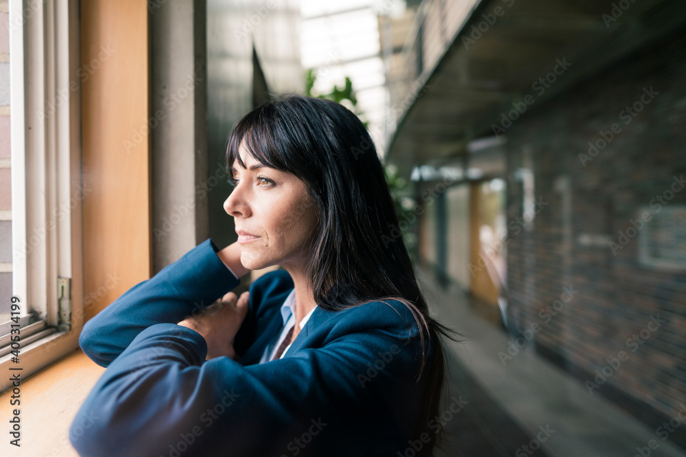 Female entrepreneur leaning while looking through window at office Female entrepreneur leaning while looking through window at office