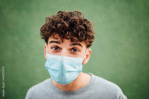 Young man with surgical mask against green background photo