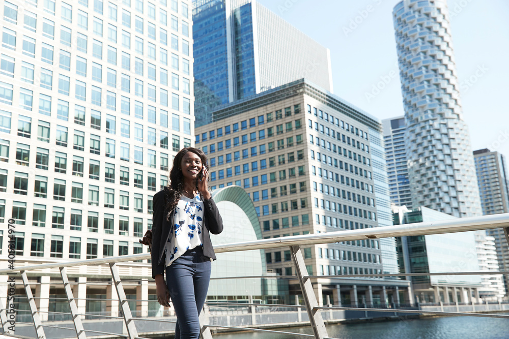 Smiling businesswoman talking on call while walking by railing on sunny day Smiling businesswoman talking on call while walking by railing on sunny day