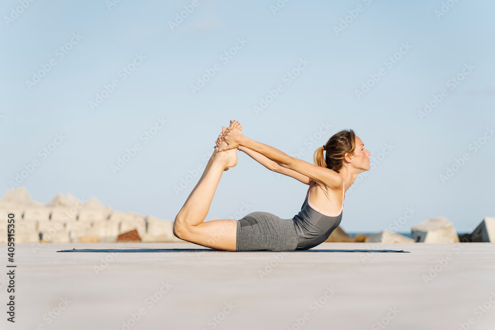 Sportswoman doing bow pose on sunny day