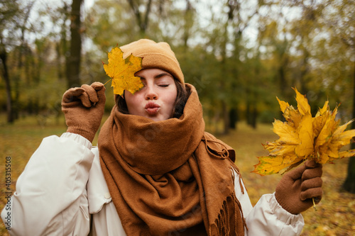 Young woman with eyes closed puckering while covering eye with autumn leaf in public park