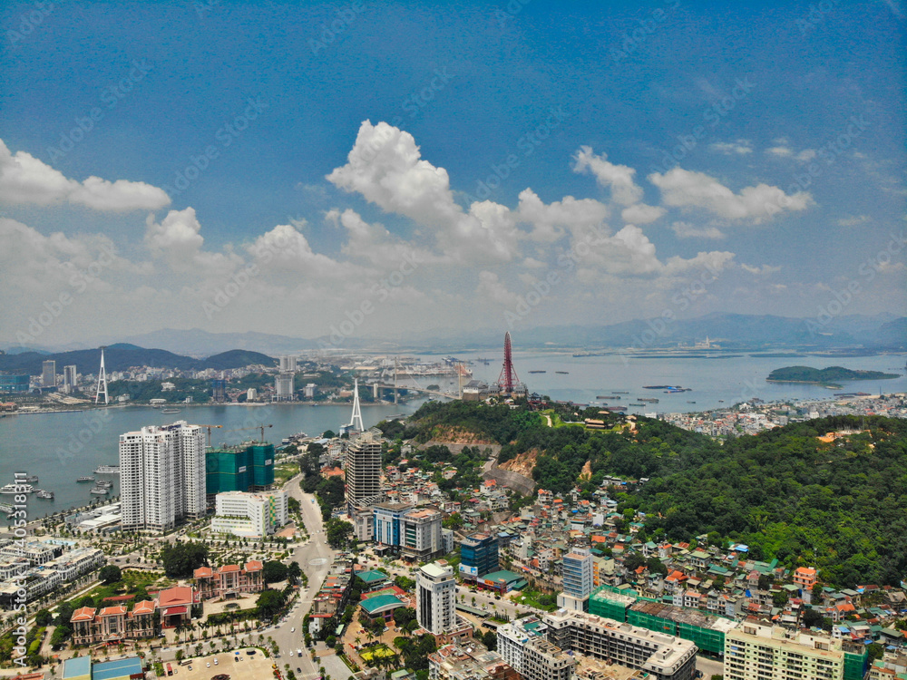 Naklejka premium Aerial view of Ha Long City skyline with Bai Chay Bridge, construction cranes, and Ha Long Bay islands in Quang Ninh, Vietnam