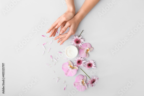 Female hands with cream and beautiful flowers on light background