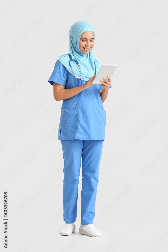 Portrait of female Muslim doctor with tablet computer on light background