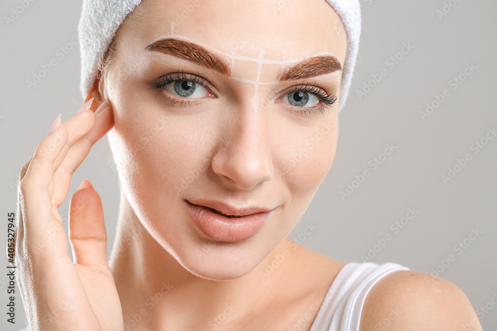 Young woman with marking for eyebrows correction against grey background Young woman with marking for eyebrows correction against grey background
