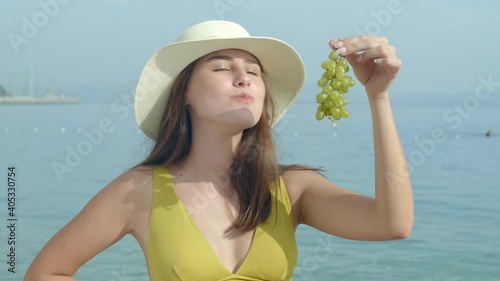 Beautiful woman in a straw hat and bikini is eating grapes on the beach.Woman eating grapes.