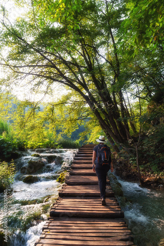 Quadro su tela Woman traveler walking on wooden path trail with lakes and waterfall landscape i