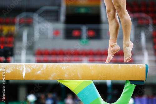 Balance beam artistic gymnastics competition performance. Close up detail of woman athlete feet on air, jump training session exercise at an indoor sport stadium arena. 