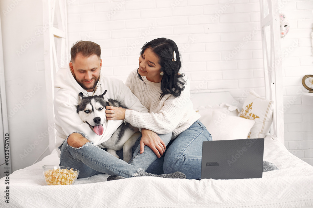 Cute couple in a bedroom. Lady in a white sweater. Pair watching a movie with a dog