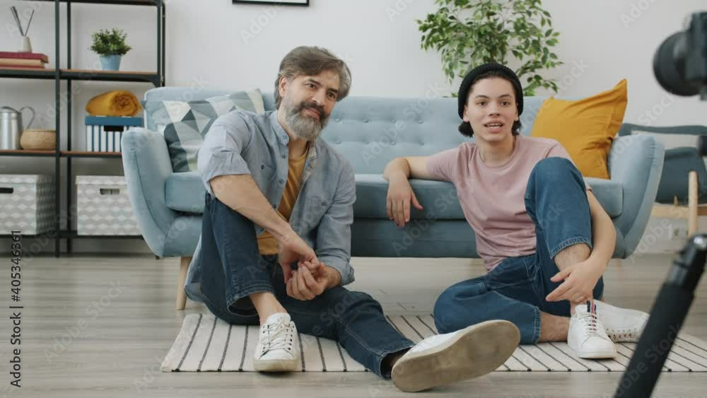 Father and son vloggers are recording video for online vlog speaking using camera sitting on floor at home. Vlogging and family relations concept. Father and son vloggers are recording video for online vlog speaking using camera sitting on floor at home. Vlogging and family relations concept.