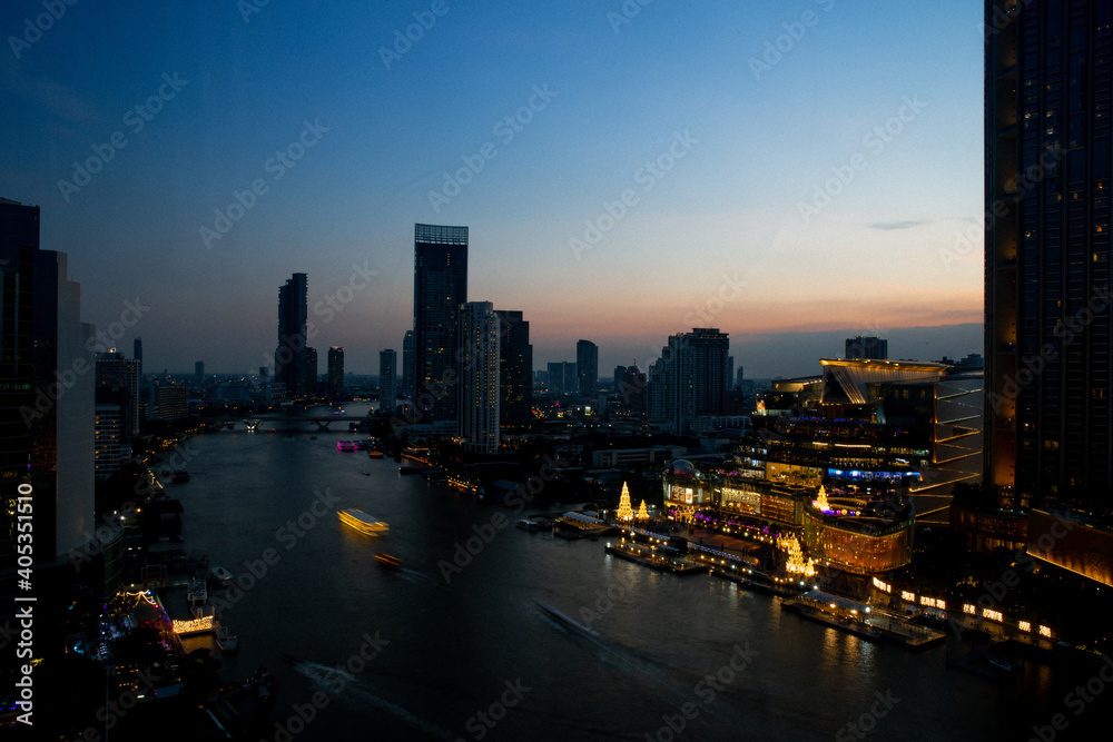 Obraz premium The Chao Phraya River flows through Bangkok in the Sathorn area, with bridges over the river and boats when the sun is setting.