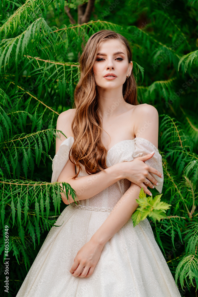 beautiful woman in a white dress posing in against of green leaves. beautiful woman in a white dress posing in against of green leaves.