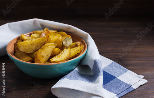 Slices of baked potatoes with herbs in a plate on a kitchen towel and a wooden table. Horizontal orientation, no people, copy space, close-up