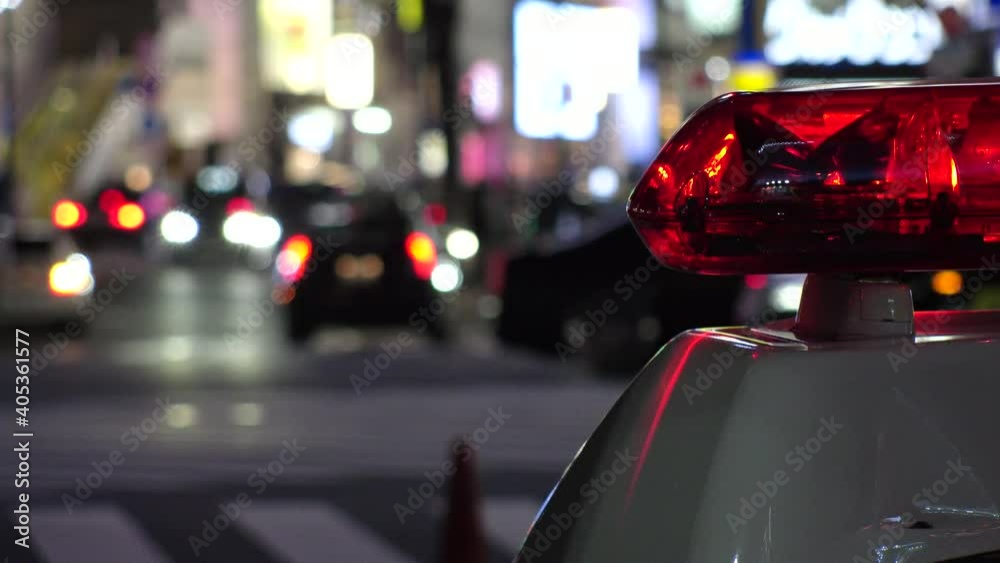 SHIBUYA, TOKYO, JAPAN - JAN 2021 : View of Police car with red beacon light at night downtown city. Crowd of people and street traffic at Shibuya crossing in background. Crime and emergency concept. SHIBUYA, TOKYO, JAPAN - JAN 2021 : View of Police car with red beacon light at night downtown city. Crowd of people and street traffic at Shibuya crossing in background. Crime and emergency concept.