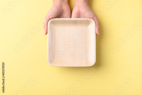 Hand holding betal palm leaf plate (Biodegradable, Compostable, Disposable or Eco friendly plate) on yellow background, Sustainable concept photo