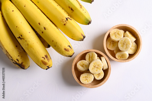Sliced ripe banana fruit in a wooden bowl and bunch of ripe banana on white backgrount, Top view