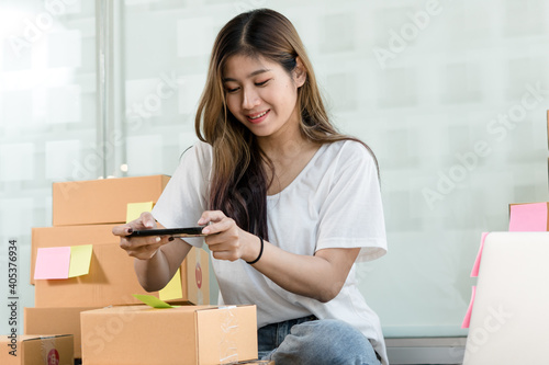 The Asian owner takes pictures of a brown package to verify his customer's address and make arrangements for delivery online while he works at home.