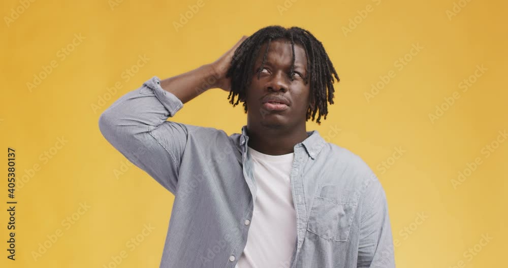 Pensive black guy with dreadlocks thinking, scratching his head and thinking, orange studio background Pensive black guy with dreadlocks thinking, scratching his head and thinking, orange studio background