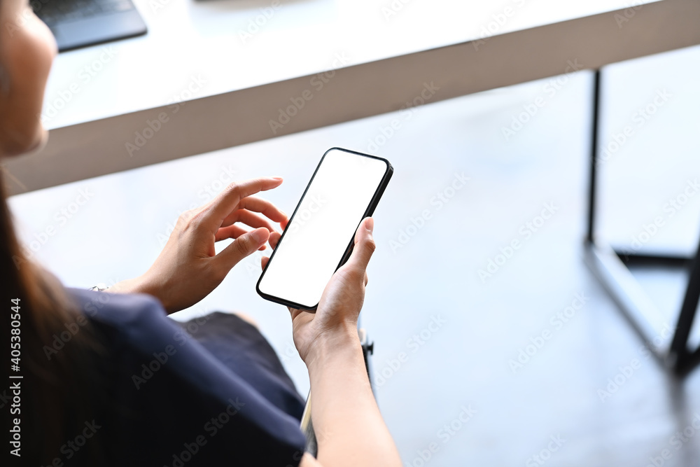 Close up view young woman sitting in modern office and holding mock. up mobile phone with blank screen.