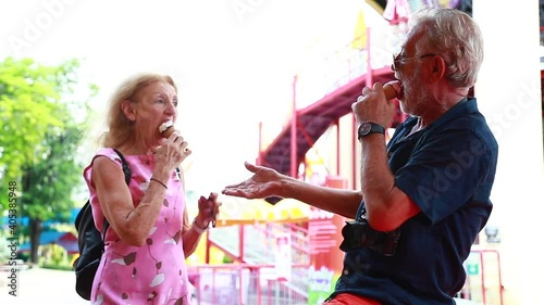 Eat ice cream cone. Happy Elderly cacasian couple dance and eat ice cream at  amusement park. Summer travel trip. Slow motion video. photo