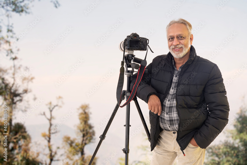 A SENIOR ADULT MAN POSING HAPPILY WITH CAMERA ON HILLTOP	