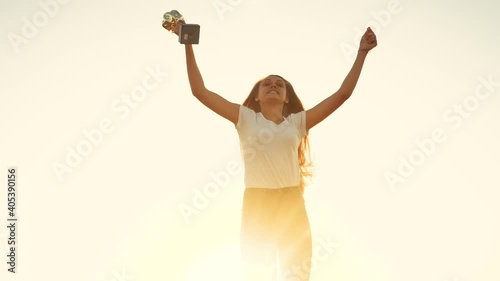 teen girl celebrating winner victory success. silhouette of happy girl athlete sportsman with cups in hand jumping rejoices. kid dream winner concept. people in the park. girl with cup trophy in hand photo