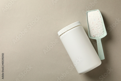 Plastic bottle and scoop with washing powder on gray background