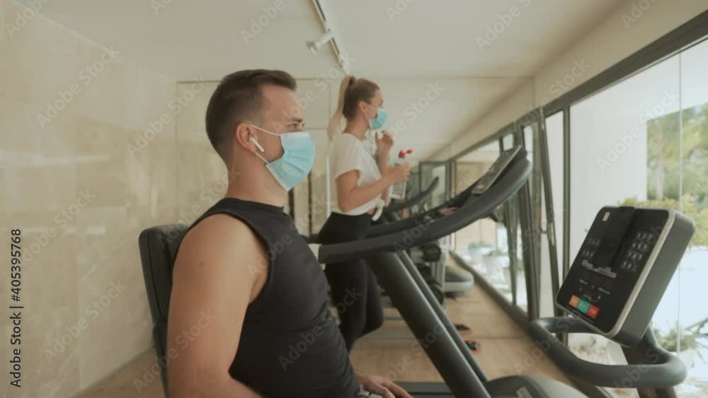 Sport during the COVID-19 pandemic. Athlete male and female with face mask using exercise machines in the gym. Sport during the COVID-19 pandemic. Athlete male and female with face mask using exercise machines in the gym.