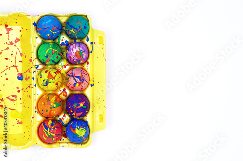 Colorful Easter eggs painted with gouache in yellow egg box isolated on white background, top view copy space 
