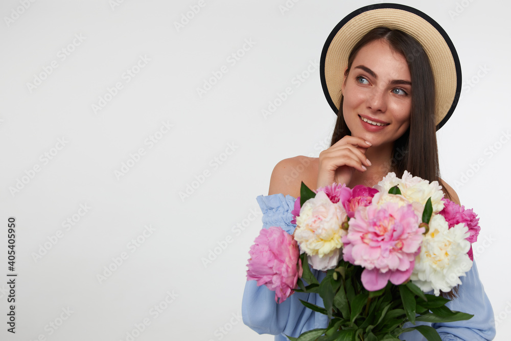 Young lady, pretty woman with long brunette hair. Wearing a hat and blue dress. Holding bouquet of flowers and touching her chin, dreaming. Watching to the left at copy space over white background Young lady, pretty woman with long brunette hair. Wearing a hat and blue dress. Holding bouquet of flowers and touching her chin, dreaming. Watching to the left at copy space over white background