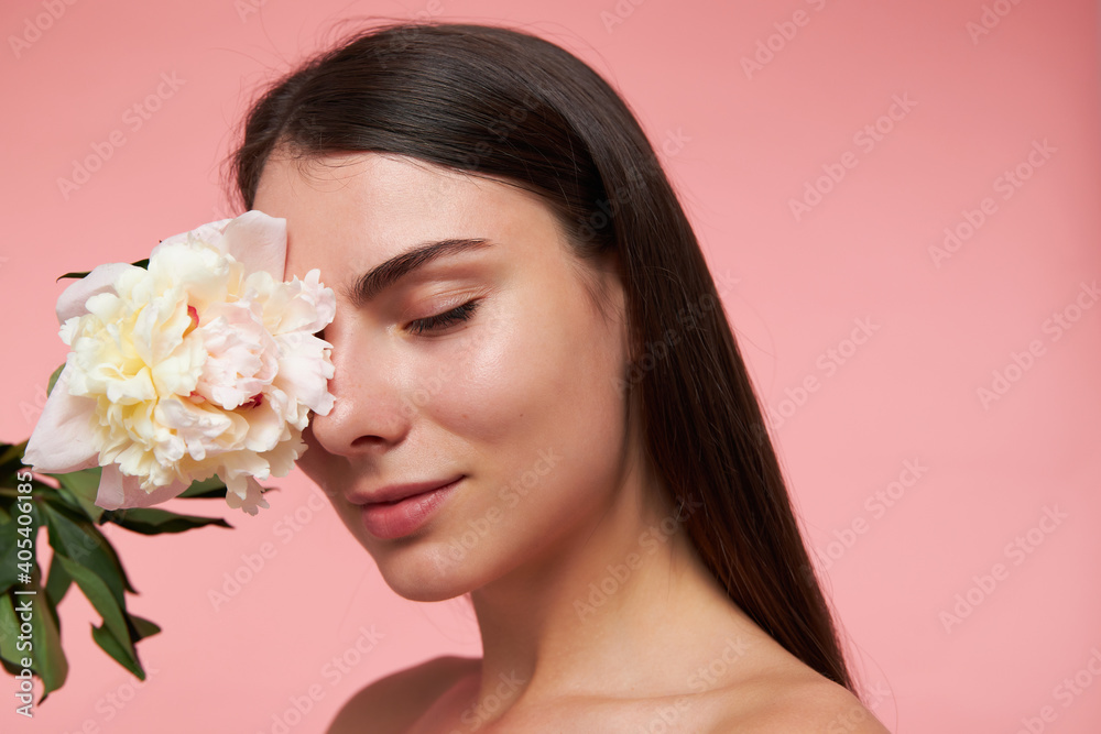Portrait of attractive, nice looking girl with long brunette hair and healthy skin, touching her eye with a flower, dreaming with closed eyes. Stand isolated, closeup over pastel pink background Portrait of attractive, nice looking girl with long brunette hair and healthy skin, touching her eye with a flower, dreaming with closed eyes. Stand isolated, closeup over pastel pink background