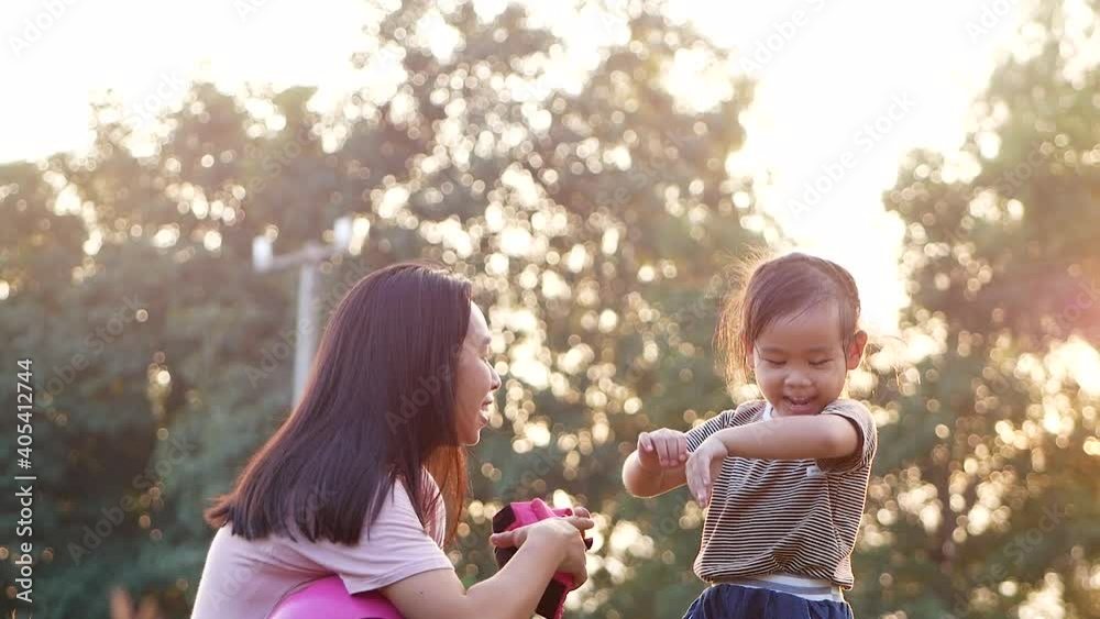 Young mother helps her daughter remove protective elbow pad after learning to ride scooter in summer park. Active outdoor sport for kids. Young mother helps her daughter remove protective elbow pad after learning to ride scooter in summer park. Active outdoor sport for kids.