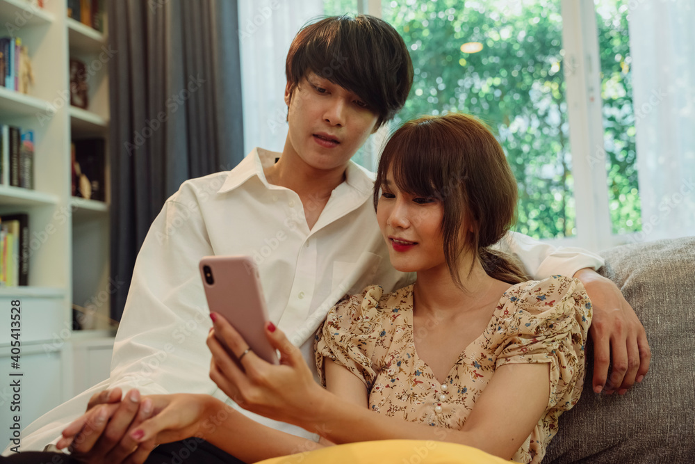Asian thai couple holding hand checking wedding program on smartphone at living room.