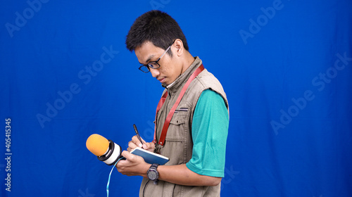 asian male journalist wear vest and ready writting for news isolated blue background