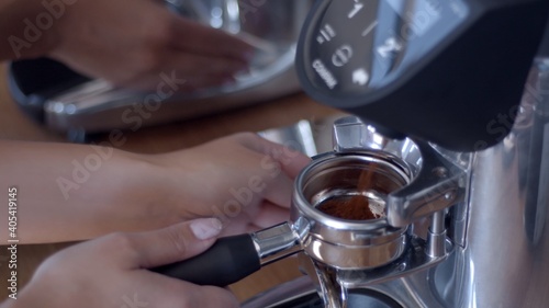 Caucasian white woman's barista hand inserting double portafilter in the grinder to collect fresh ground specialty coffee to make espresso. Professional grinder. High-quality jpg image close-up © Anastasia