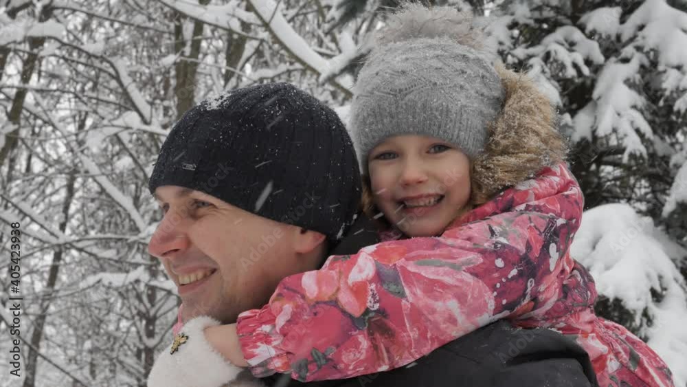 Happy adorable baby girl child sitting on father's shoulders in the park in winter season. Father and daughter standing while snow falling in the forest. Happy adorable baby girl child sitting on father's shoulders in the park in winter season. Father and daughter standing while snow falling in the forest.
