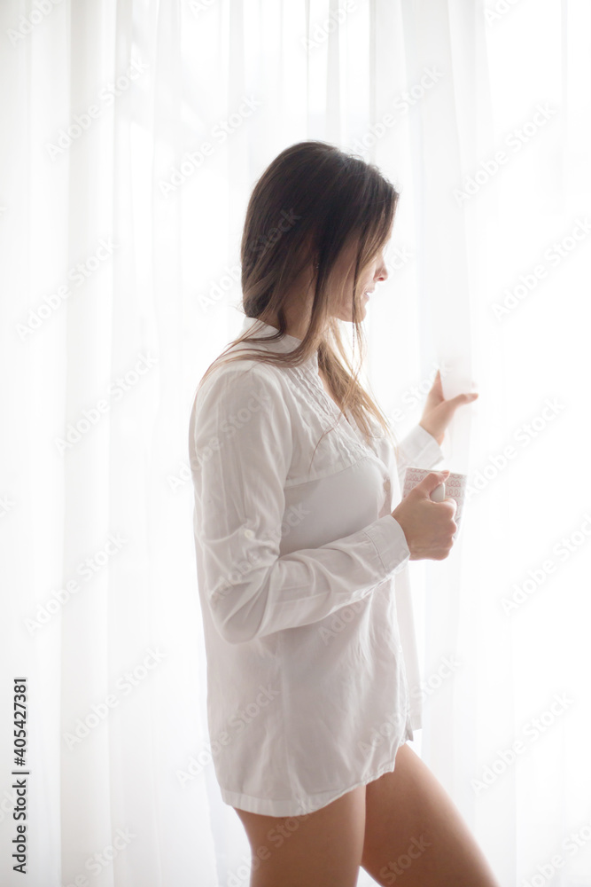 Middle age woman with white dress, drinking coffee at home, looking out of the window Middle age woman with white dress, drinking coffee at home, looking out of the window