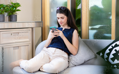 Portrait Young caucasian woman massaging checking social media on mobile phone while sitting a couch at home.