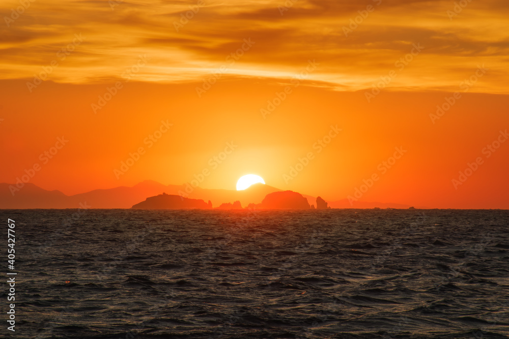 Watching a golden sunset with the sun hiding behind far away rocks into the sea  from Parikia, Paros island Greece.