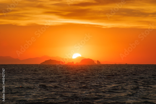 Watching a golden sunset with the sun hiding behind far away rocks into the sea  from Parikia  Paros island Greece.