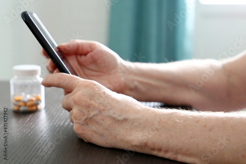 Elderly woman with smartphone sitting at the table, mobile phone in wrinkled female hands. Concept of online communication at retirement, search for disease symptoms