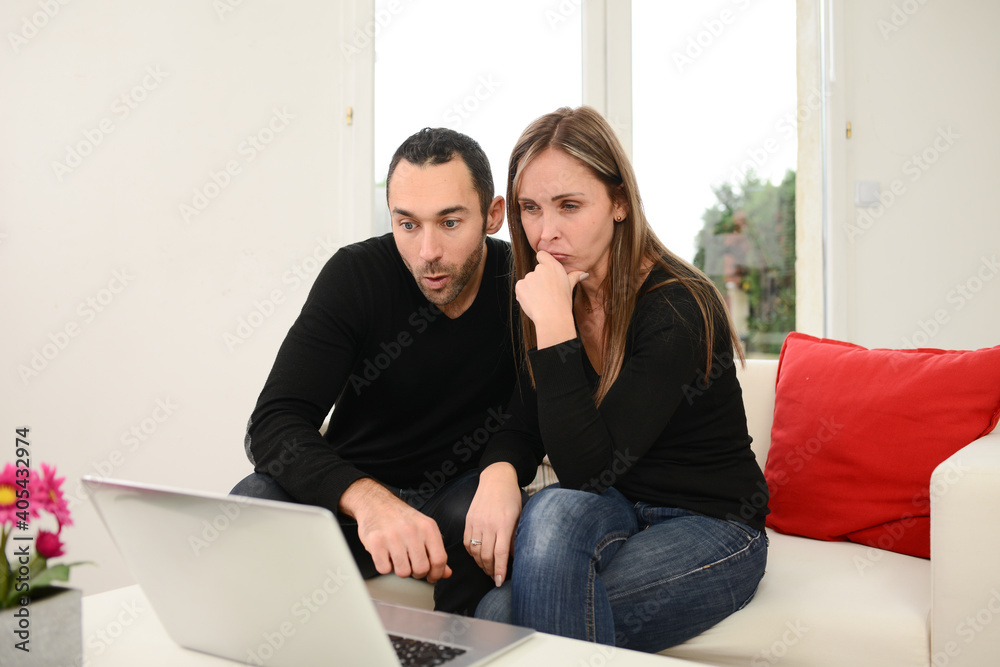 Beautiful couple making shopping internet web browsing search on their computer laptop in the living room Beautiful couple making shopping internet web browsing search on their computer laptop in the living room