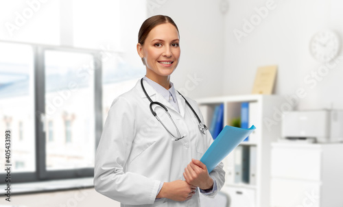 medicine, profession and healthcare concept - happy smiling female doctor in white coat with folder and stethoscope over hospital background