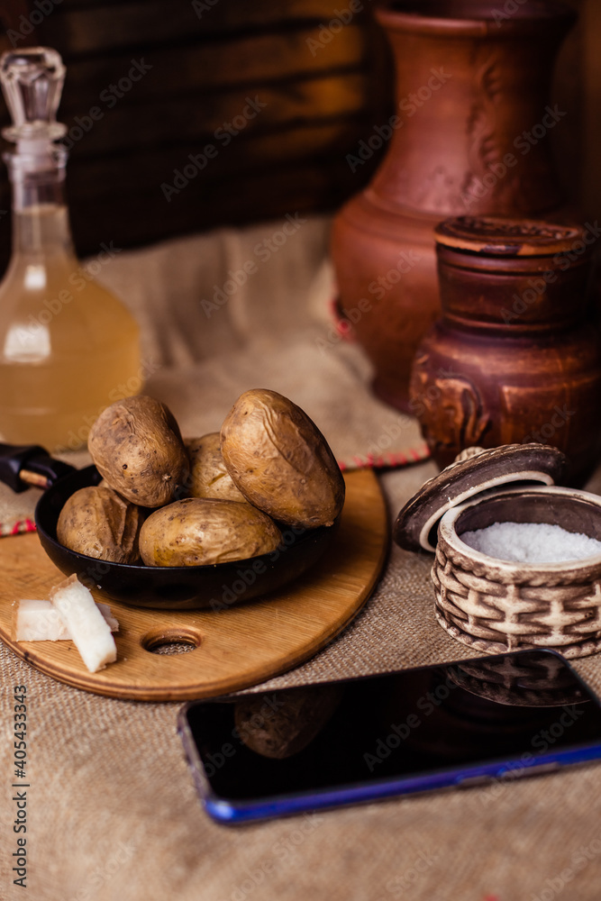 Boiled fresh potatoes in uniform on a wooden board in a cast-iron pan. Russian cuisine. Dinner in the Russian village. salt are on the table. On the background of clay pots Boiled fresh potatoes in uniform on a wooden board in a cast-iron pan. Russian cuisine. Dinner in the Russian village. salt are on the table. On the background of clay pots