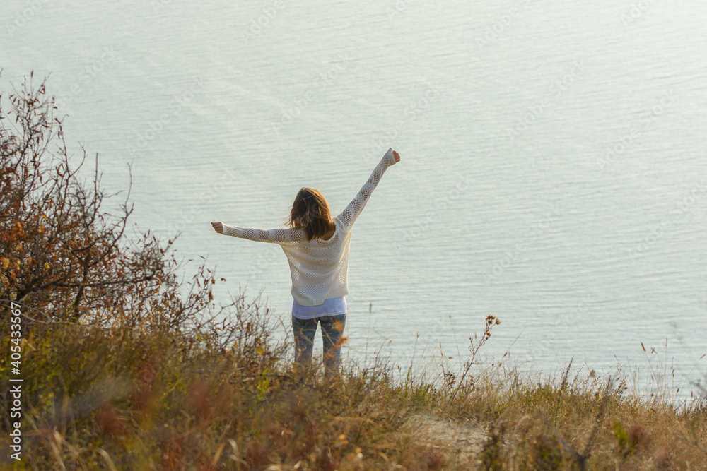 Happy girl happily raised her hands up enjoying the seascape, view from the back Happy girl happily raised her hands up enjoying the seascape, view from the back