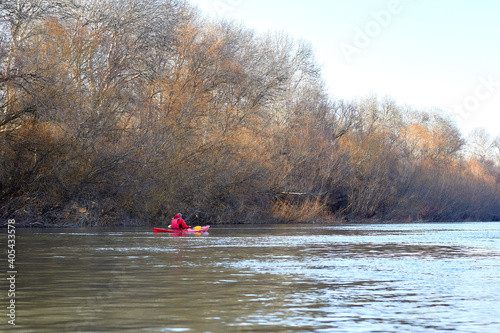 Man paddles red kayak on the Danube river near trees in fall season