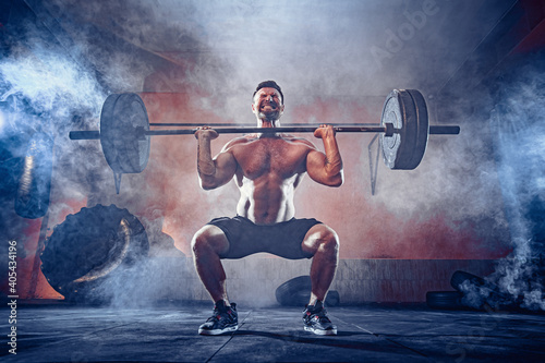 Muscular fitness man doing deadlift a barbell over his head in modern fitness center. Functional training. Snatch exercise. Smoke on background.