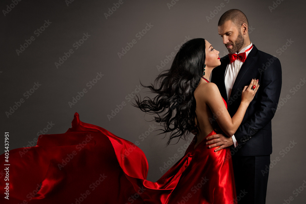 Fototapeta Lovely Happy Couple dancing. Woman in red Dress and Man in Black Suit with Bow Tie. Flying silk Fabric and hair on Wind. Studio Background