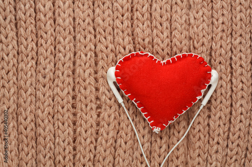 Red heart sewn from fabric on a knitted background with headphones. Valentine day card